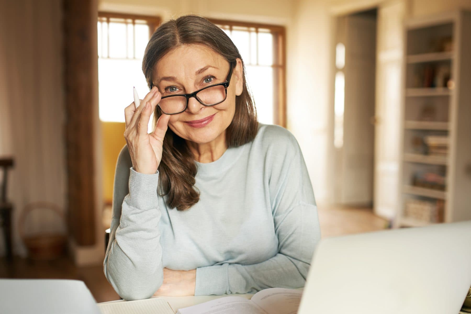 A homeowner at her laptop reviewing paperwork at home, lowering her glasses
