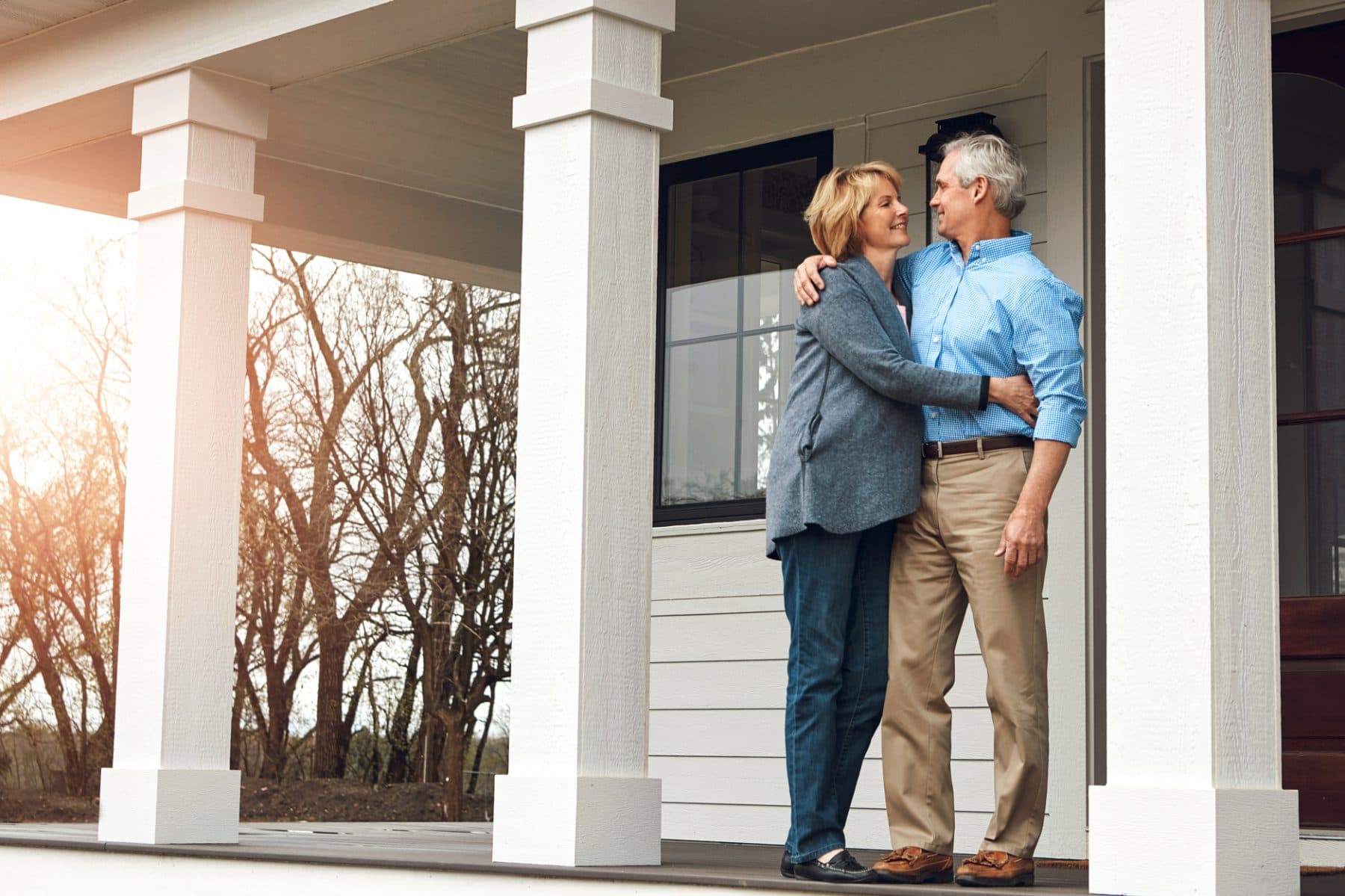 An older couple embracing on the front porch of their home at golden hour