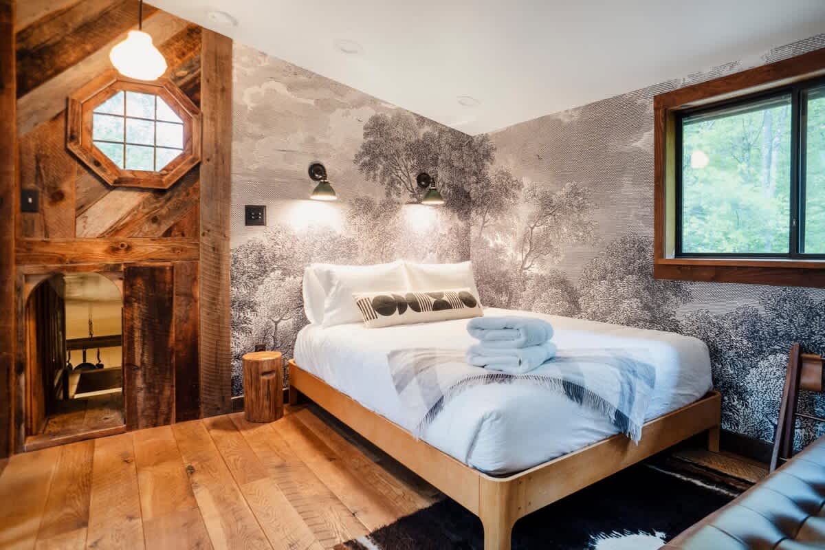 A bedroom at 1392 Route 214 with botanical mural wallpaper, reclaimed wood trim, and a wooded view