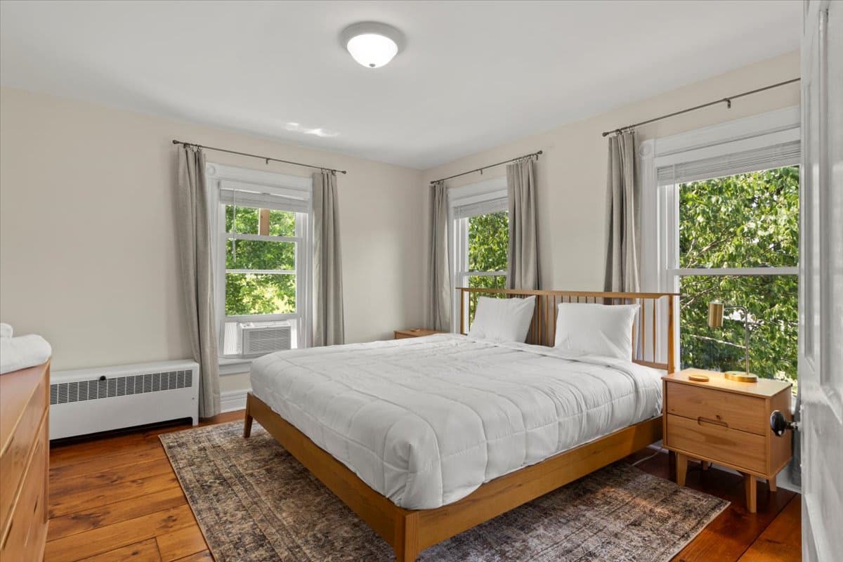 A light-filled bedroom at 725 Route 66 with wood floors and three windows onto green trees