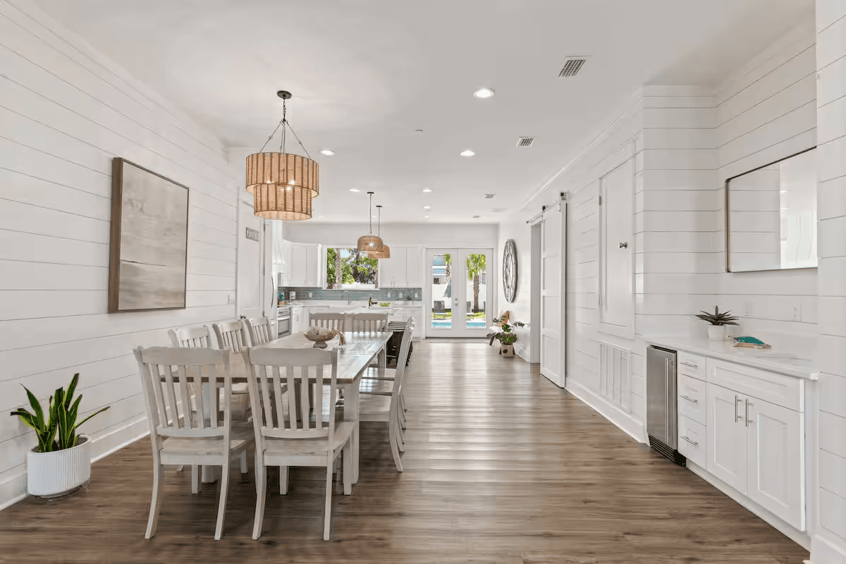 The open dining and kitchen area at 103 Shirah with shiplap walls, a long farmhouse table, and a view to the pool